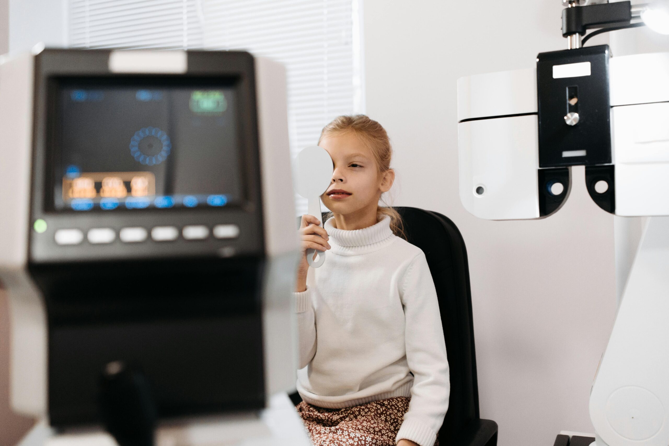 Young girl covering one eye during an optometric exam in a clinic setting.
